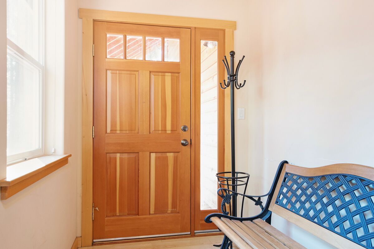 A wooden door with a window above it, a bench with a blue backrest, and a metal coat rack.