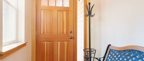 A wooden door with a window above it, a bench with a blue backrest, and a metal coat rack.
