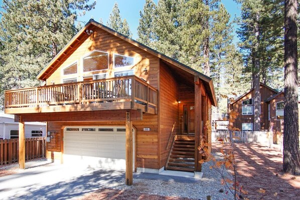A two-story wooden cabin with a balcony, a garage, and a staircase leading to the upper floor.