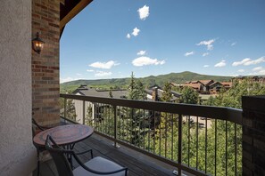 A balcony with a table and chairs, overlooking a mountainous landscape with buildings.