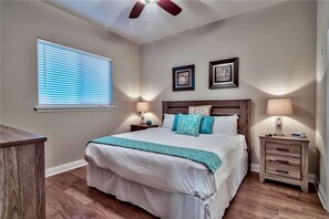 Cozy retreat with a large bed, bedside tables, and a ceiling fan, featuring a window with blinds and a framed picture on the wall.