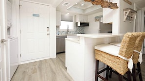 Une cuisine moderne avec des meubles blancs, un four à micro-ondes encastré et un bar en bois avec des chaises en osier.