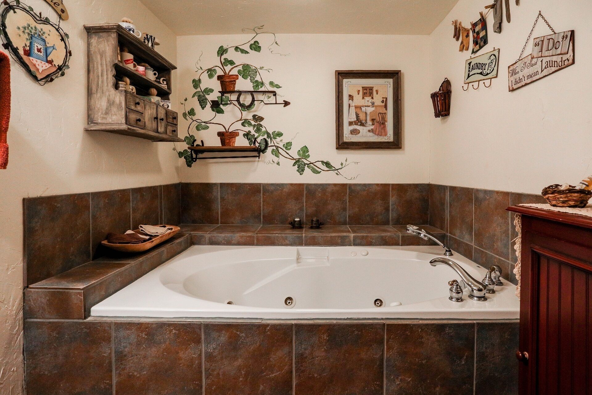 Un baño con una bañera grande, paredes con azulejos, un estante de madera con adornos y un cuadro en la pared.