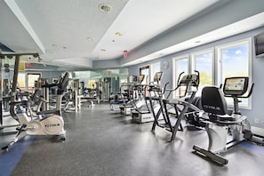 A gym with various exercise machines, large windows, and a mirrored wall.