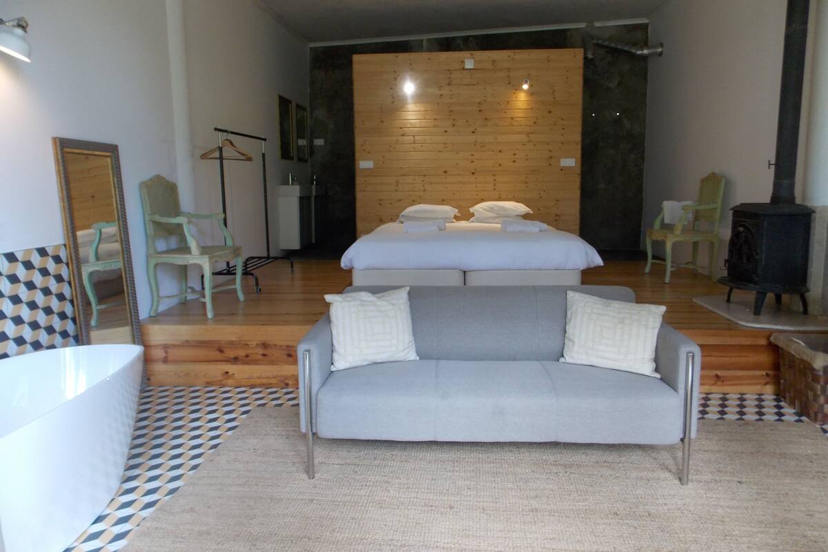 A modern bedroom with a large bed, a grey sofa, and a wooden wall.