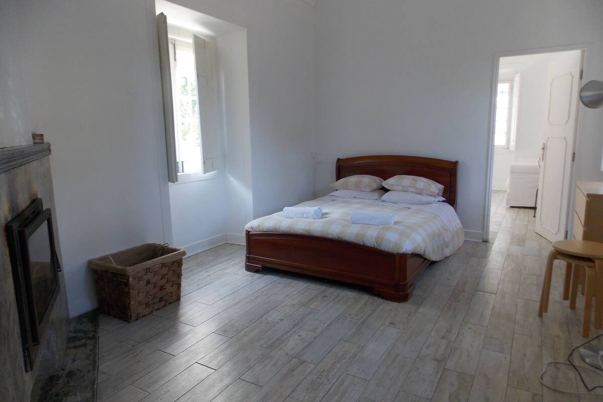 A bedroom with a wooden bed, a small window, a fireplace, and a wooden floor.