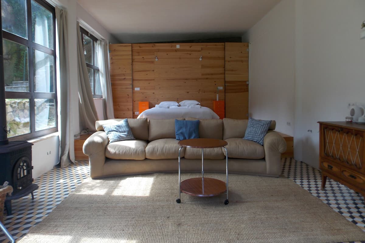 A cozy room with a large window, a wooden headboard, a sofa, a small round table, and a checkered floor.