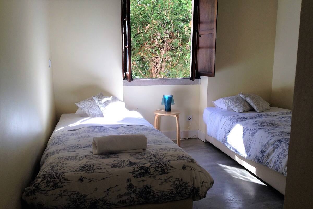 A room with two beds, a small table, and a window with curtains.