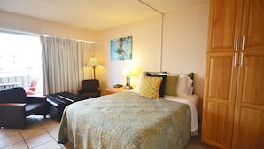 Habitación de hotel con cama, una silla, un escritorio, una lámpara y un cuadro en la pared.