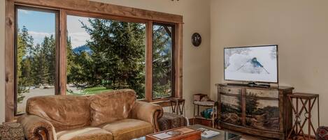 A living room with a leather sofa, a glass coffee table, a television, and a cabinet with a painting.