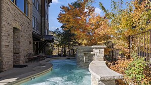A spa area with a hot tub, stone walls, and a view of a building with large windows.