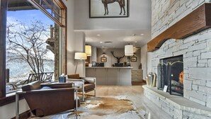 A modern living room with a stone fireplace, leather sofas, and a large window overlooking a snowy landscape.