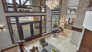 A spacious living area with a large window, a chandelier, and a stone wall.