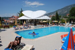 Un espace piscine aménagé avec des chaises longues, des parasols et une grande tente blanche.