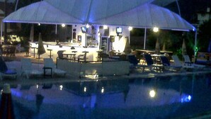 A poolside bar area with tables and chairs, a pool, and umbrellas providing shade.