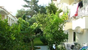A residential area with a narrow pathway, lush greenery, and a building with balconies.