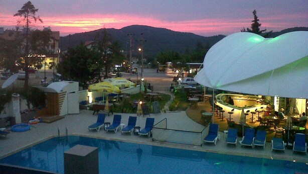 A resort pool area with lounge chairs, a covered seating area, and mountains in the background.
