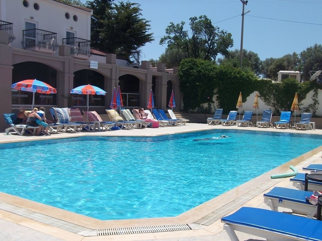 Una piscina con sillones de descanso y sombrillas, rodeada por un edificio con arcos y balcones.