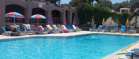 A swimming pool with lounge chairs and umbrellas, surrounded by a building with arches and balconies.