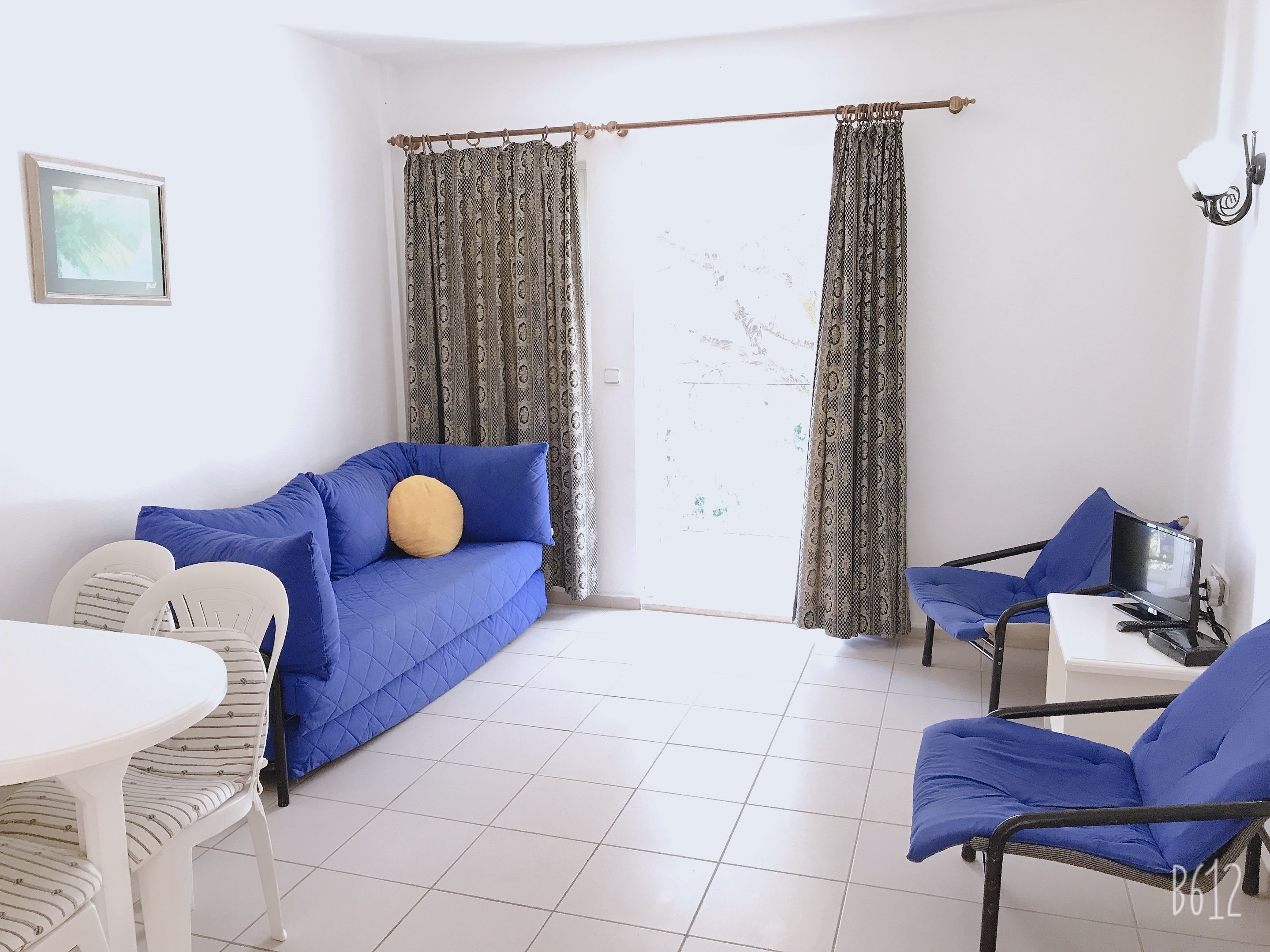 Une pièce avec un canapé bleu, une petite table, une chaise et un ordinateur portable posé sur un support.
