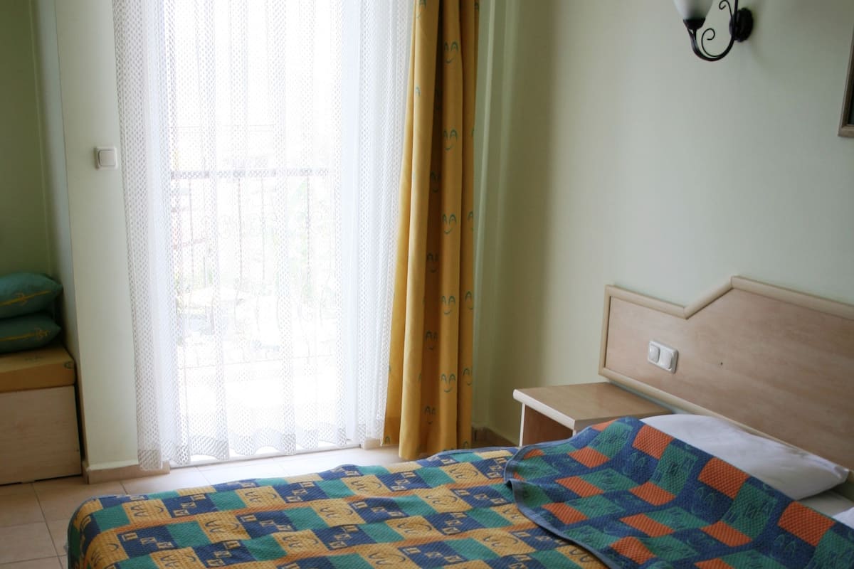 Uma cama com um edredom colorido, uma mesa de cabeceira e uma janela com cortinas.