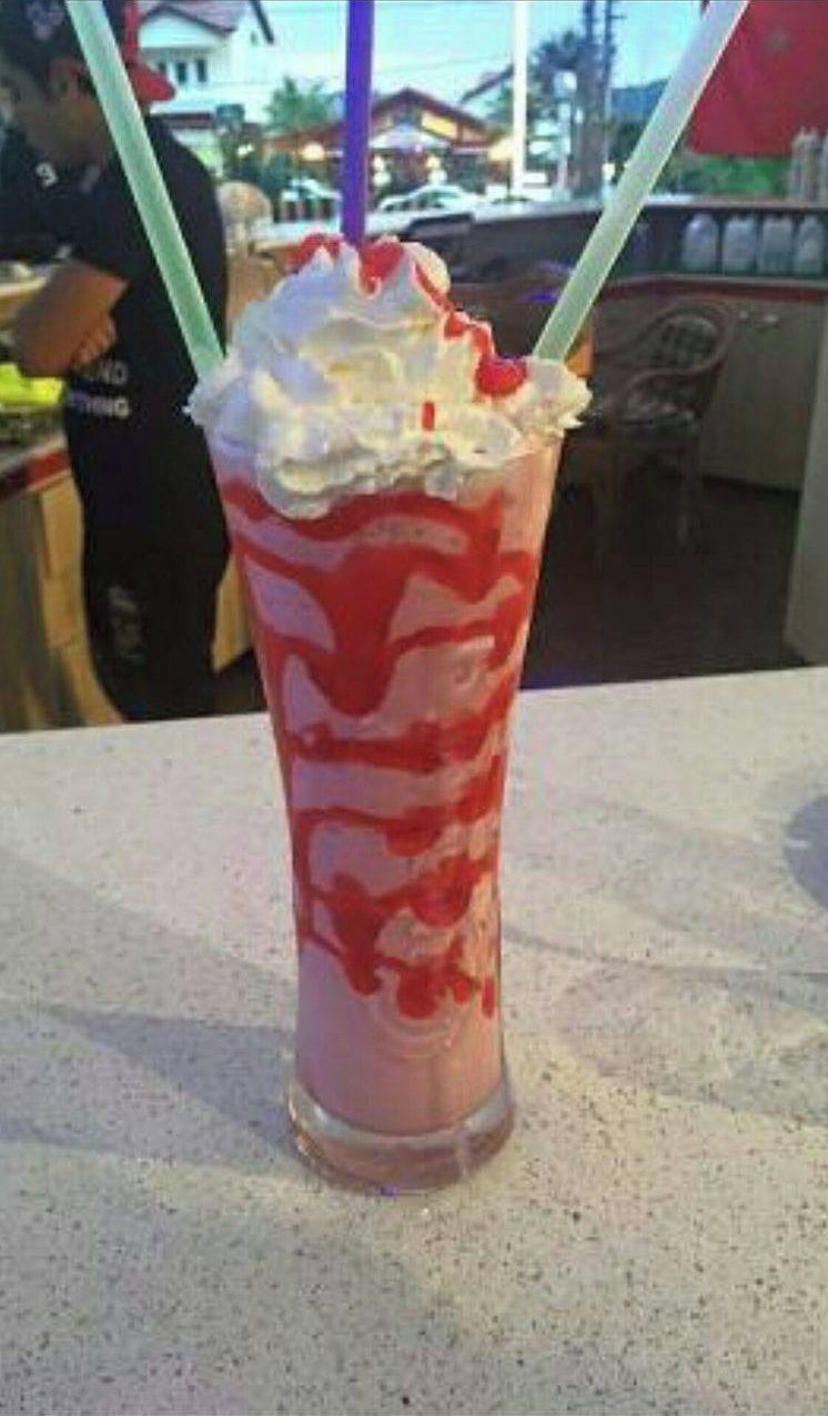 Et højt glas med en lagdelt drik, muligvis en milkshake eller smoothie, toppet med flødeskum.