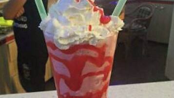 Et højt glas med en lagdelt drik, muligvis en milkshake eller smoothie, toppet med flødeskum.