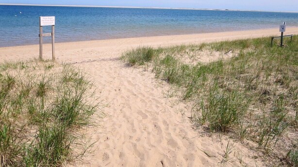A sandy beach path leading to the water with a sign indicating 'Please Respect Our Private Beach'.