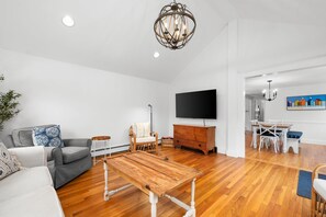 A spacious living room with a wooden coffee table, a grey sofa, a wicker chair, and a flat-screen TV mounted on the wall. - Your Perfect South Chatham Summer Stay!! (Chatham)