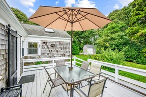 A deck with a glass table and chairs, a large beige umbrella, and a white fence. - Your Perfect South Chatham Summer Stay!! (Chatham)