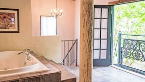 Un baño con una bañera grande, un candelabro, un cuadro enmarcado en la pared y una ventana con cortinas.