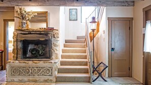 Una chimenea de piedra con un espejo encima, una escalera que sube a un segundo piso y una puerta a la derecha.