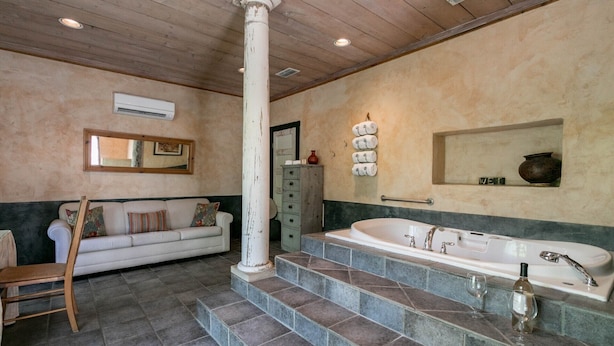 Un baño con una bañera grande, un pilar blanco, un sofá y un espejo.