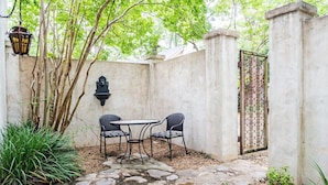 Un patio de piedra con dos sillas de mimbre y una mesa, rodeado por un muro bajo y una reja decorativa.