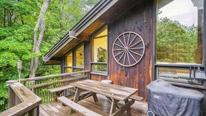A wooden deck with picnic tables and a covered grill area, surrounded by dense forest.