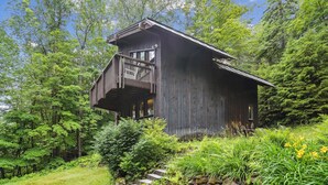 Eine rustikale Holzhütte mit Balkon, umgeben von üppigem Grün.