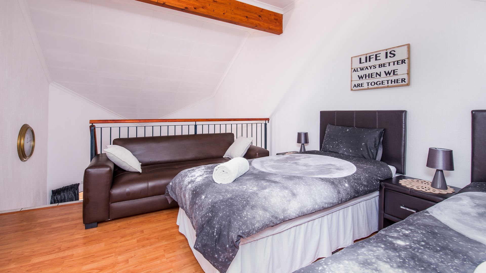 A bedroom with a brown leather sofa, a bed with a galaxy-patterned bedspread, a nightstand with a lamp, and a motivational quote on the wall.