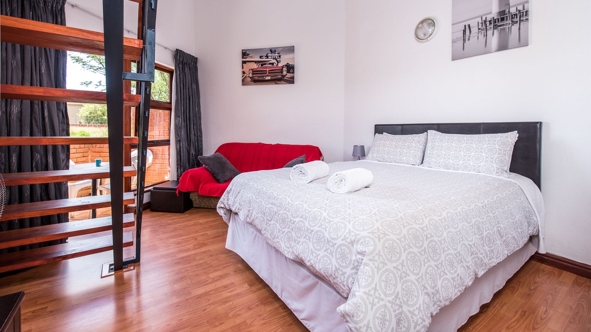 Een hotelkamer met een bed, een rode stoel, een houten trap en een aan de muur hangend schilderij.