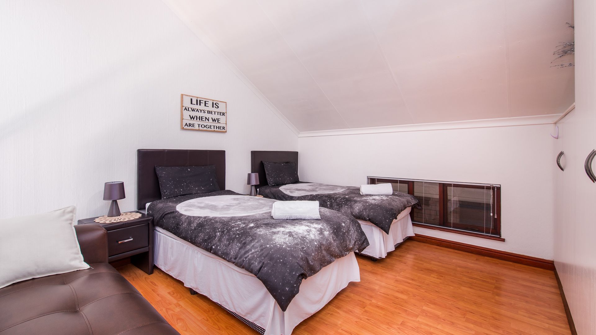 Un dormitorio con dos camas, una mesita de noche, una lámpara, un letrero en la pared y una ventana con persianas.