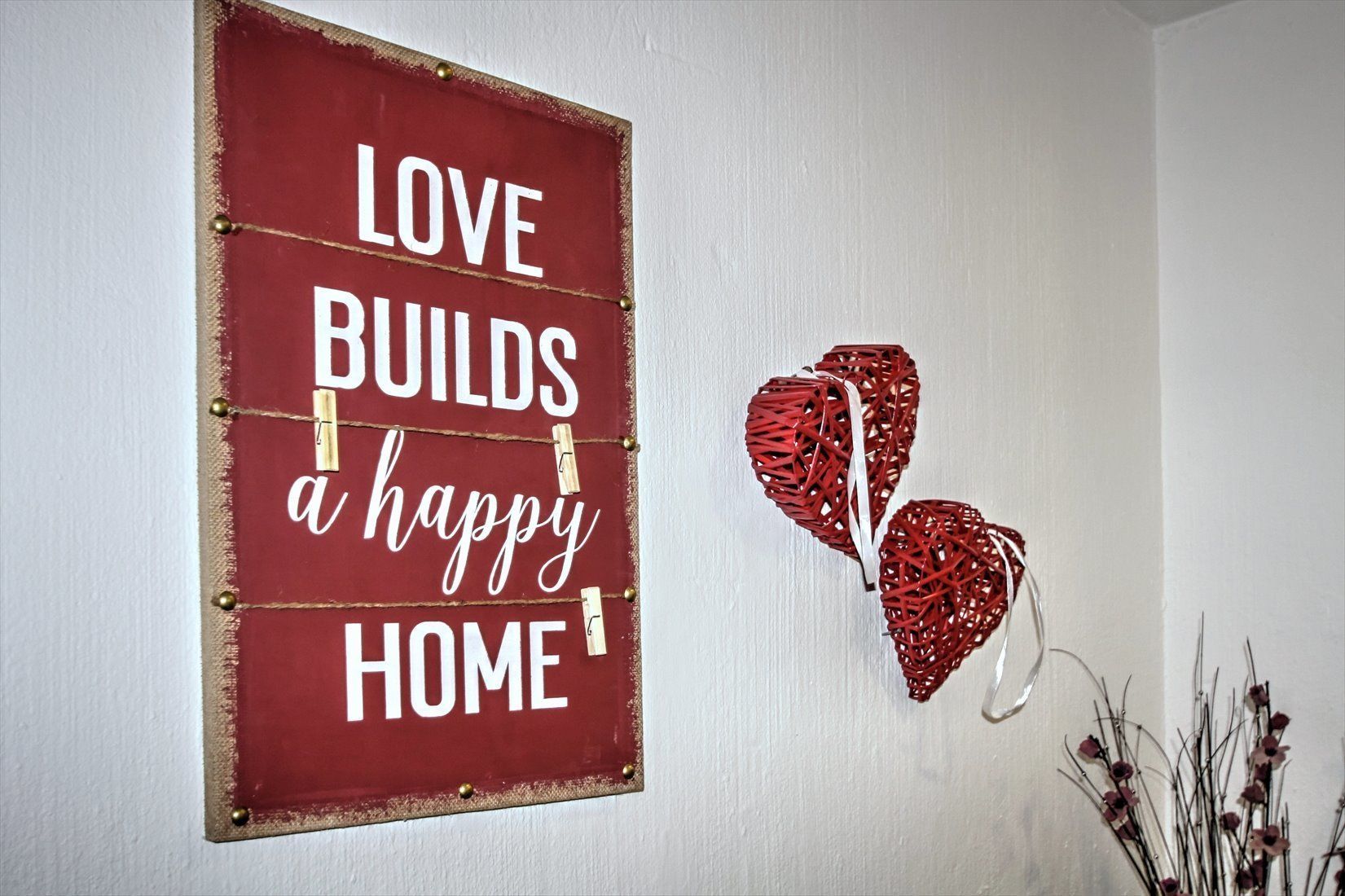 Una pared con un letrero que dice "LOVE BUILDS a happy HOME" y dos adornos con forma de corazón rojo.