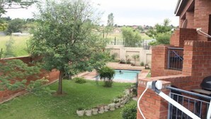 A backyard with a swimming pool, a brick wall, and a tree.
