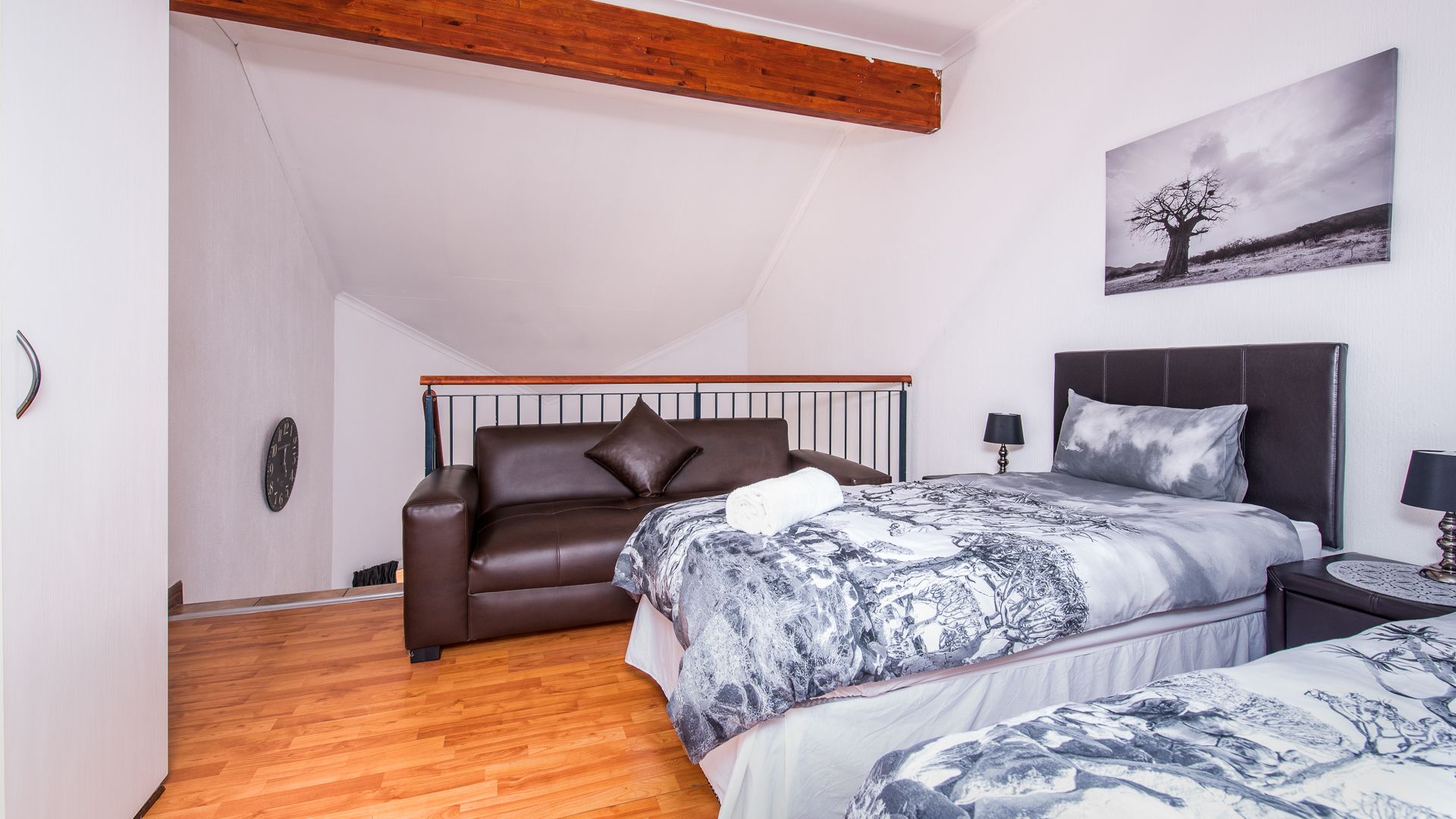 Et soveværelse med seng, sofa, et billede og et trælofts.