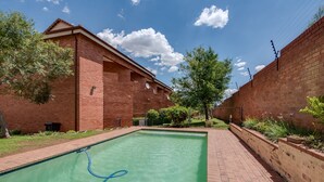 A swimming pool with a brick border, surrounded by a brick wall and greenery.