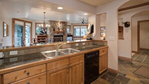 A kitchen with granite countertops, wooden cabinets, a dishwasher, and a stone fireplace. - CX324 | Large Wrap Around Balcony | Winter Shuttle | Ski In/out | Hot Tub (Steamboat Springs)