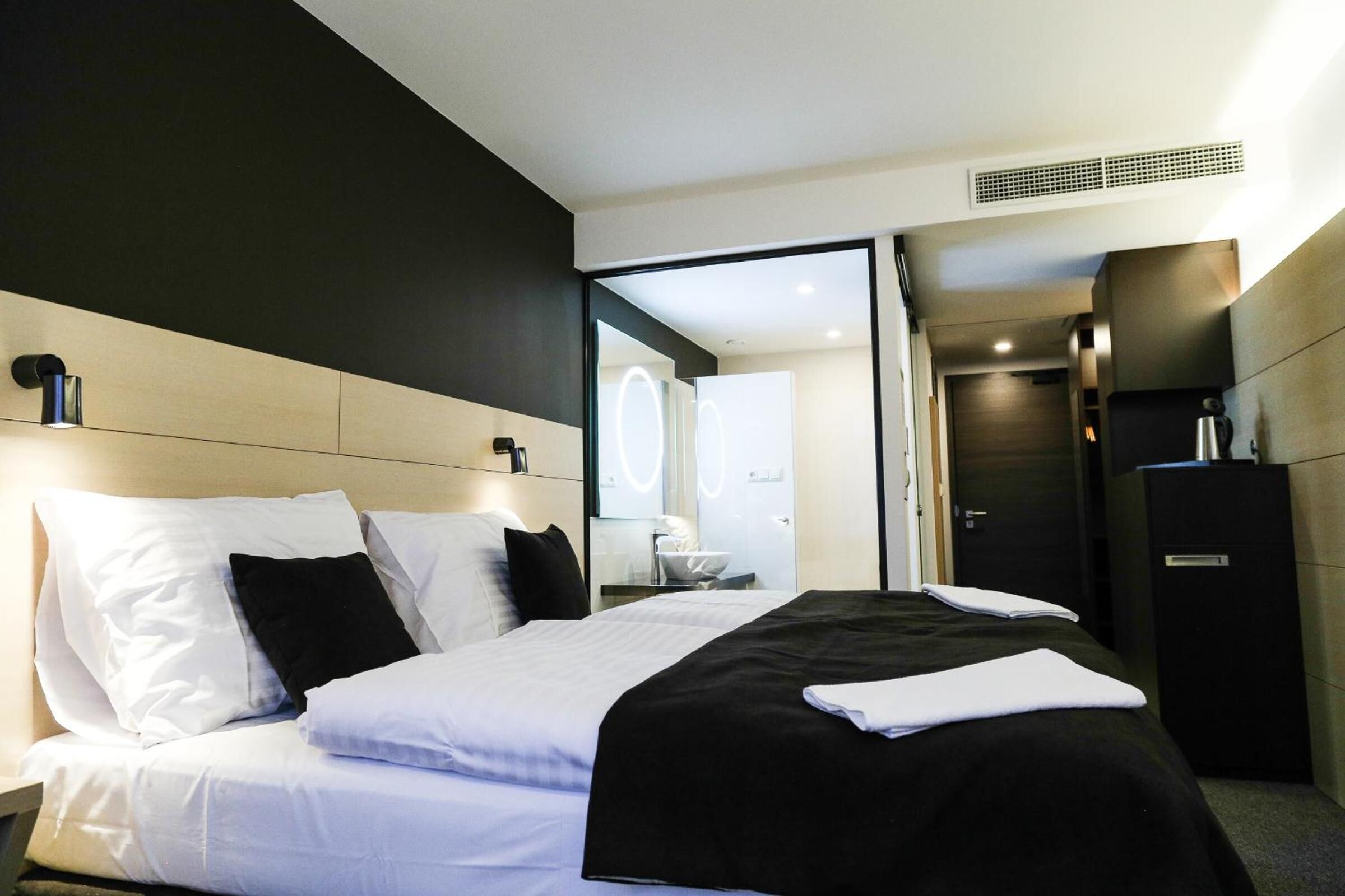 Ein modernes Hotelzimmer mit einem großen Bett, einem Schreibtisch und einem durch eine geöffnete Tür einsehbaren Badezimmer.