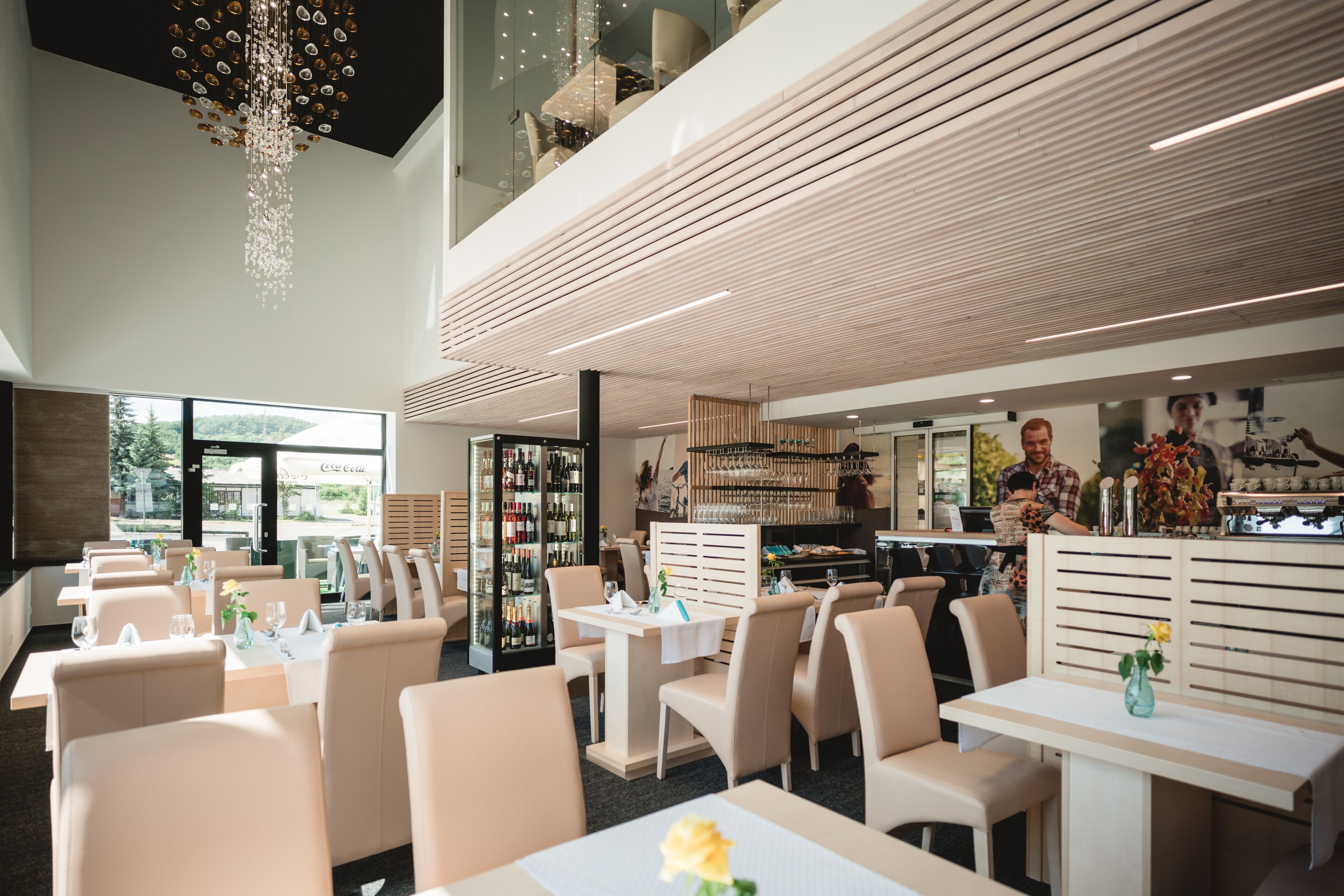 A modern restaurant with high ceilings, a chandelier, and a bar area.