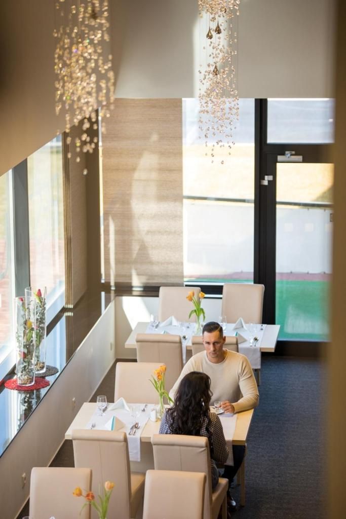 Un restaurante con mesas dispuestas para dos, ventanas amplias y lámparas colgantes.