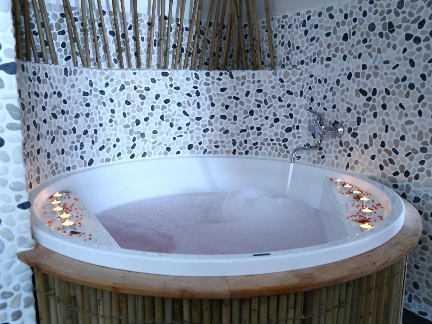Un bain à remous avec un mur décoré d’une mosaïque de galets et un décor en bambou.