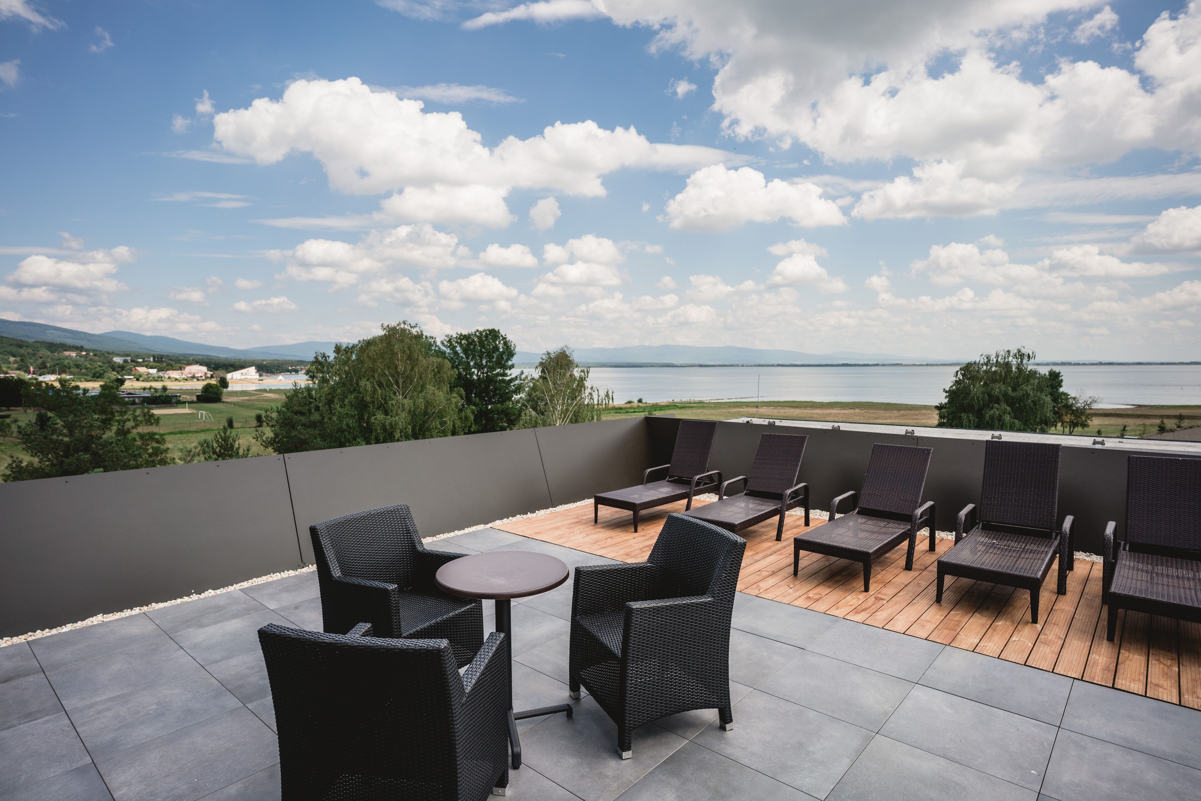 Una terraza con mobiliario de mimbre y vistas a un cuerpo de agua y un paisaje distante.