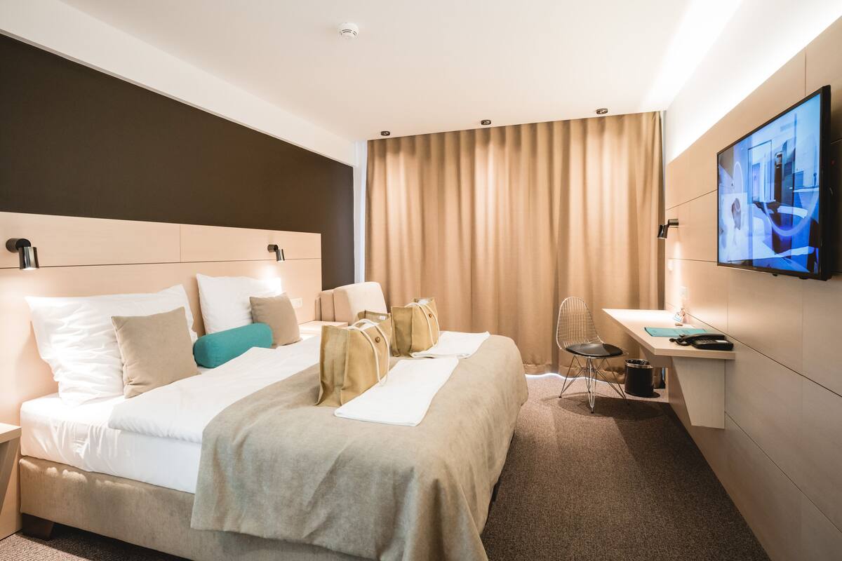 A hotel room with a bed, a desk, a chair, a television, and a curtain.